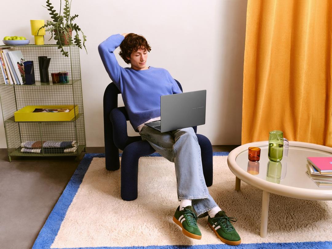 Jovem sentado em uma cadeira, usando um notebook prateado em um ambiente moderno e iluminado.