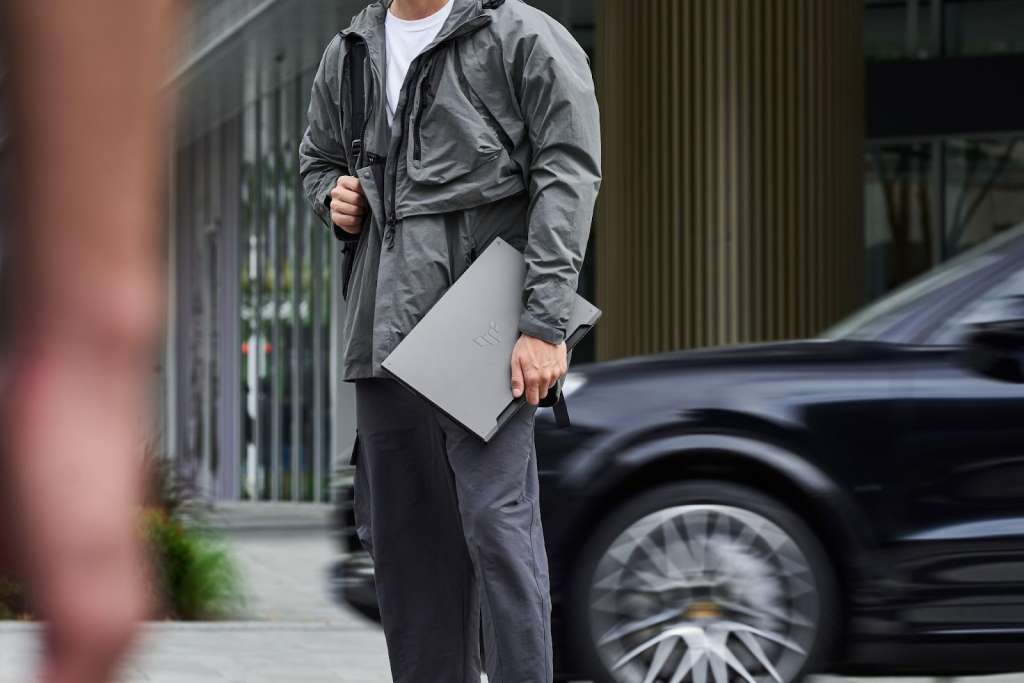 Pessoa caminhando na rua com um notebook gamer ASUS na mão, com foco no portátil e ambiente urbano.