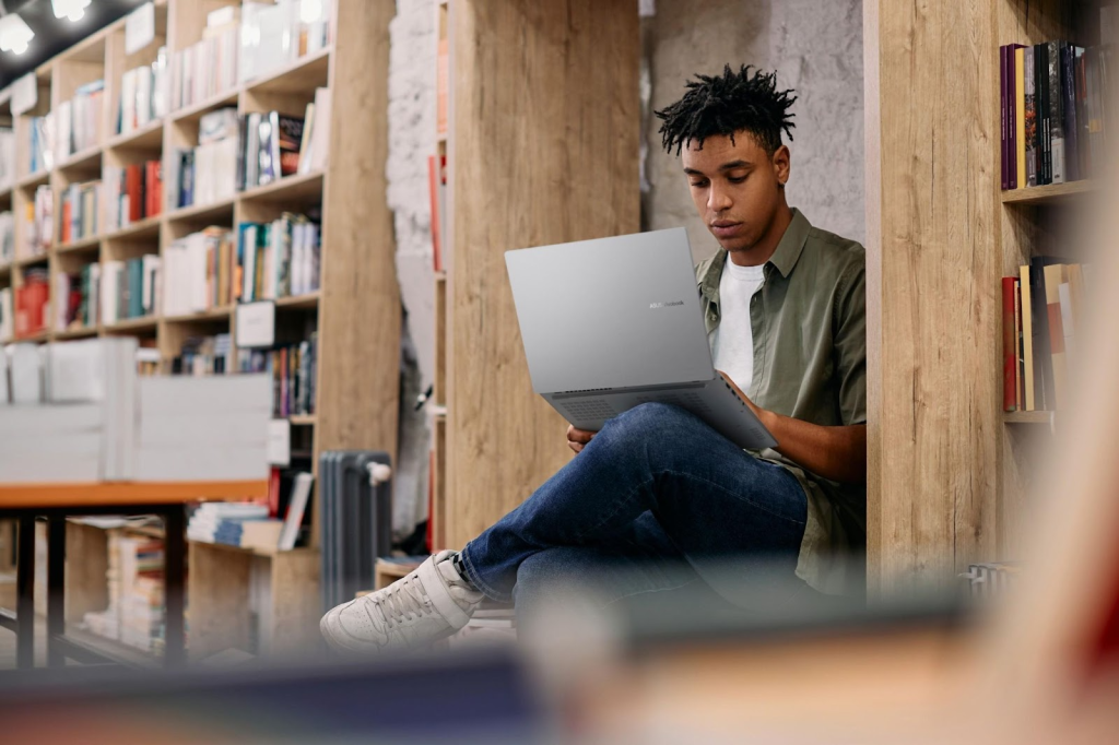 Imagem de um jovem sentado em uma biblioteca, utilizando os recursos do MyASUS para a produtividade, em um ambiente de estudo.
