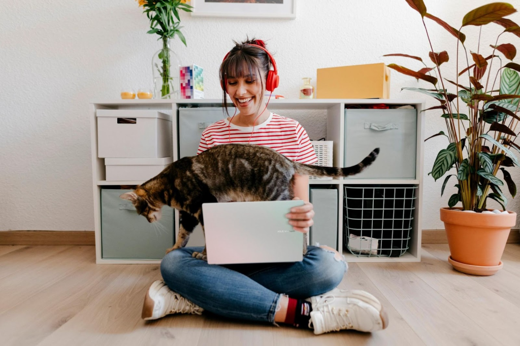 Imagem de uma jovem sorridente usando fones de ouvido e os recursos do MyASUS em seu notebook da ASUS, segurando um gato no colo.