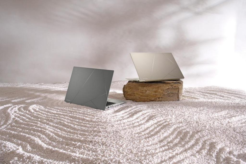 Dois notebooks modernos em acabamento de ceraluminum, um apoiado sobre uma base de madeira e outro diretamente na areia clara.