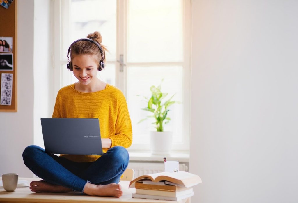 Jovem segurando um notebook ASUS e usando fones de ouvido, ilustrando a migração do windows 10 para o windows 11.