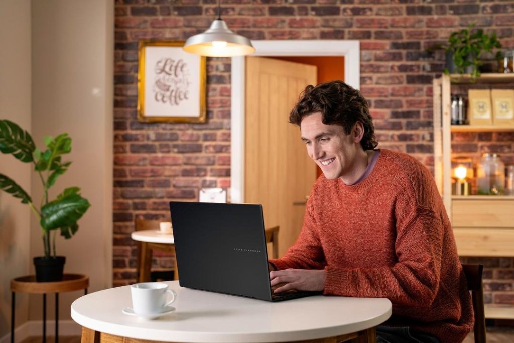 Homem sorrindo enquanto usa notebook, aproveitando o live caption para acompanhar a conversa online.