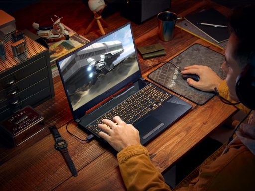 Pessoa jogando em um notebook gamer ASUS sobre uma mesa de madeira.
