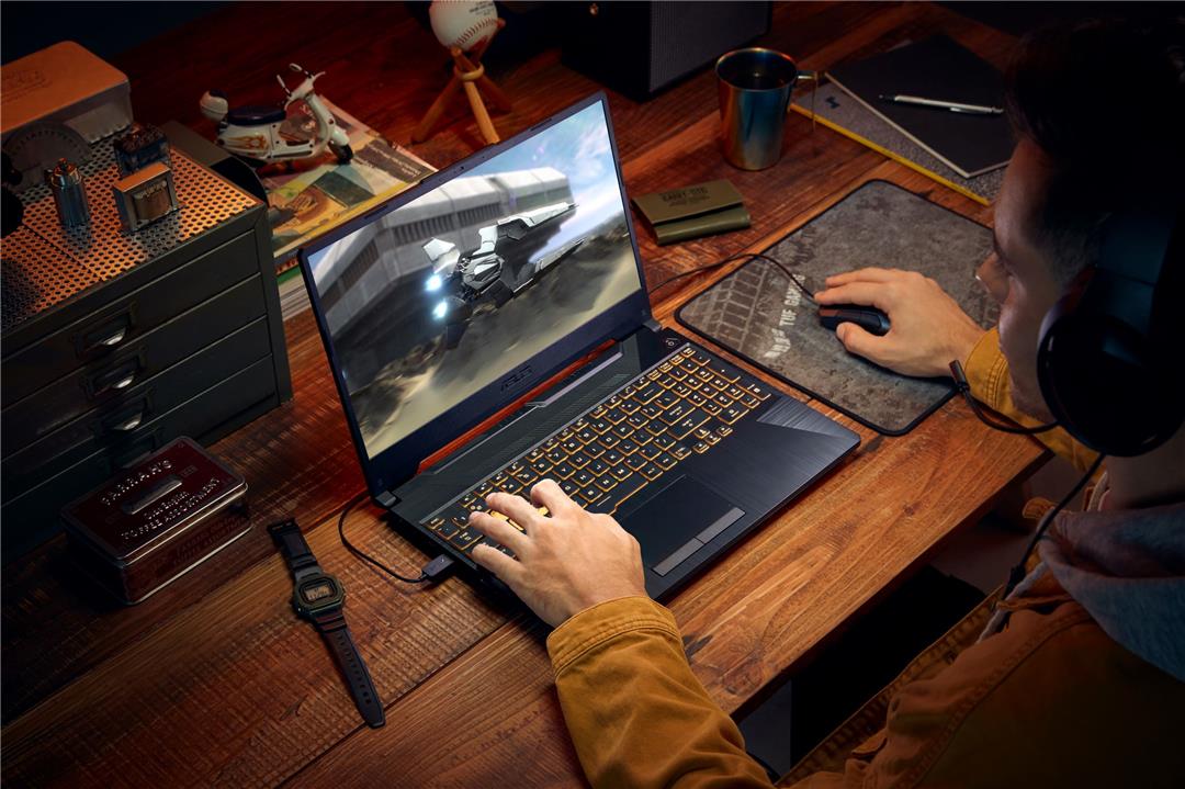 Pessoa jogando em um notebook gamer ASUS sobre uma mesa de madeira.