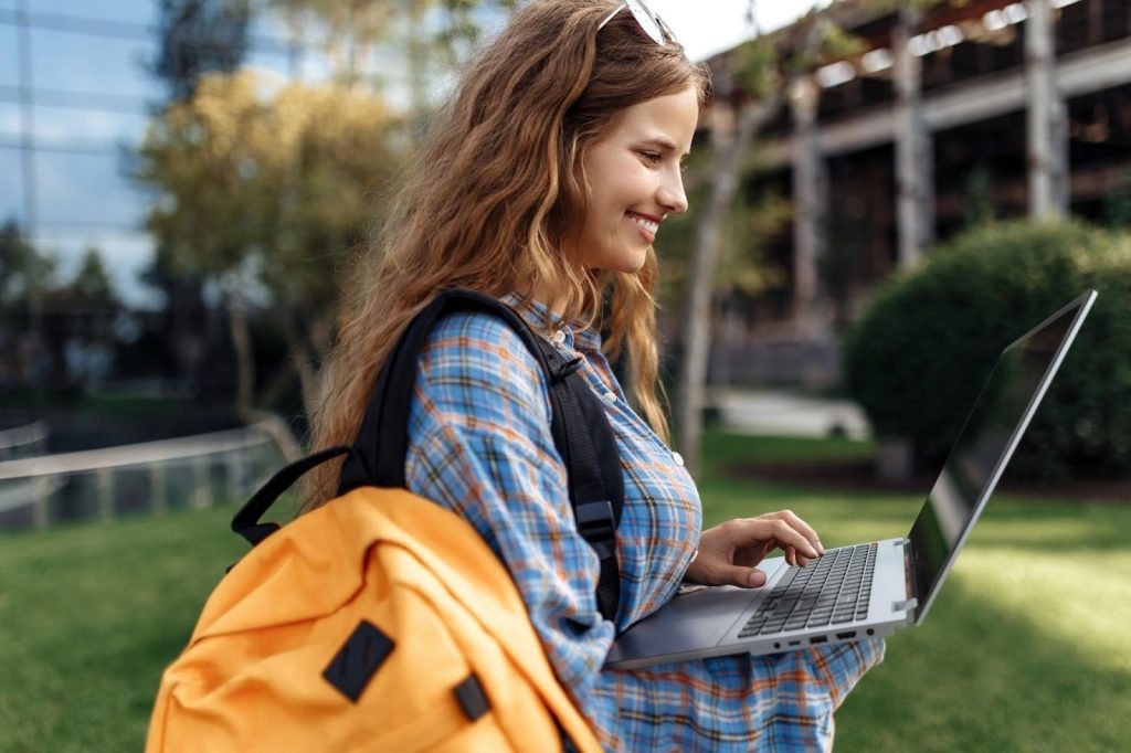 Jovem usando um notebook ao ar livre, mostrando o que é um Vivobook em termos de portabilidade e mobilidade.
