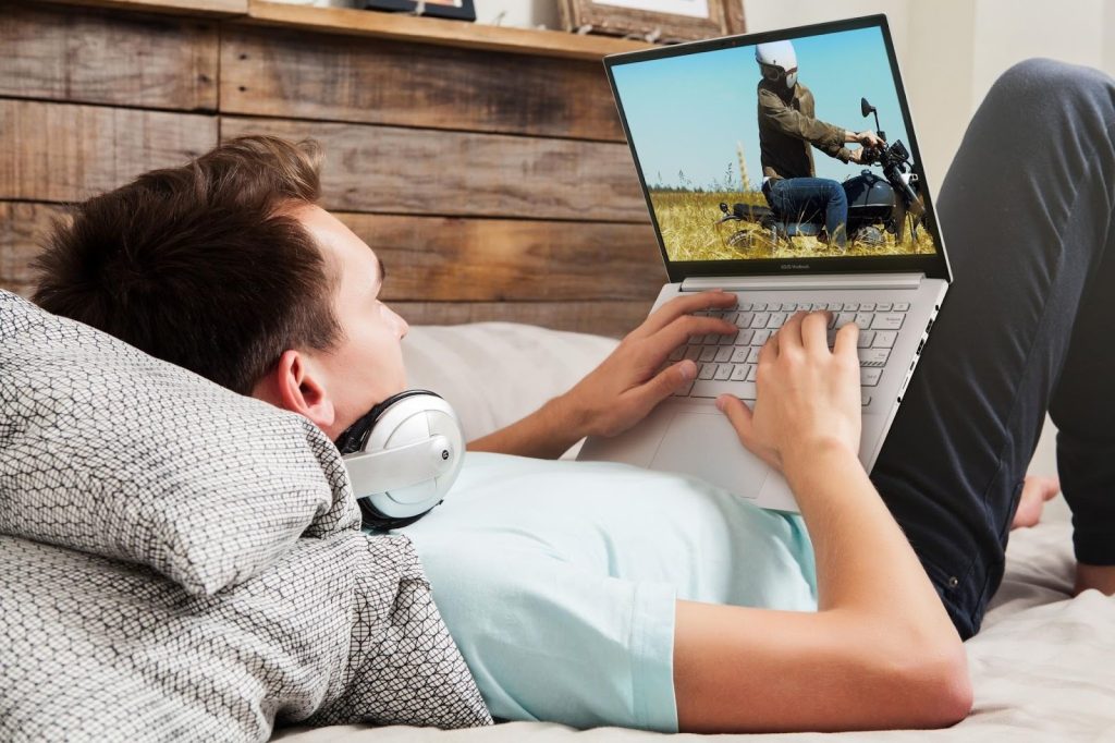 Homem deitado assistindo a vídeo em notebook representando como saber se um notebook é bom para entretenimento em casa.