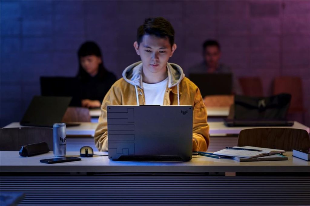 Pessoa utilizando o notebook gamer ASUS TUF Gaming A15 em sala de aula, com outras pessoas ao fundo.