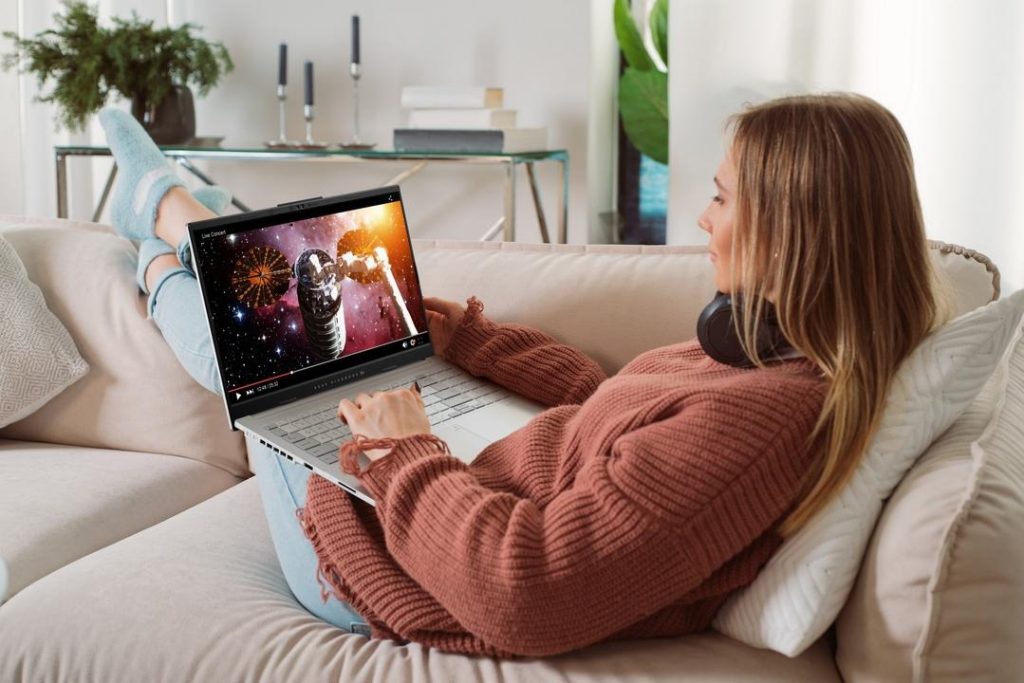 Mulher relaxada no sofá assistindo a um vídeo em seu notebook, mostrando na prática dicas de como saber se um notebook é bom.