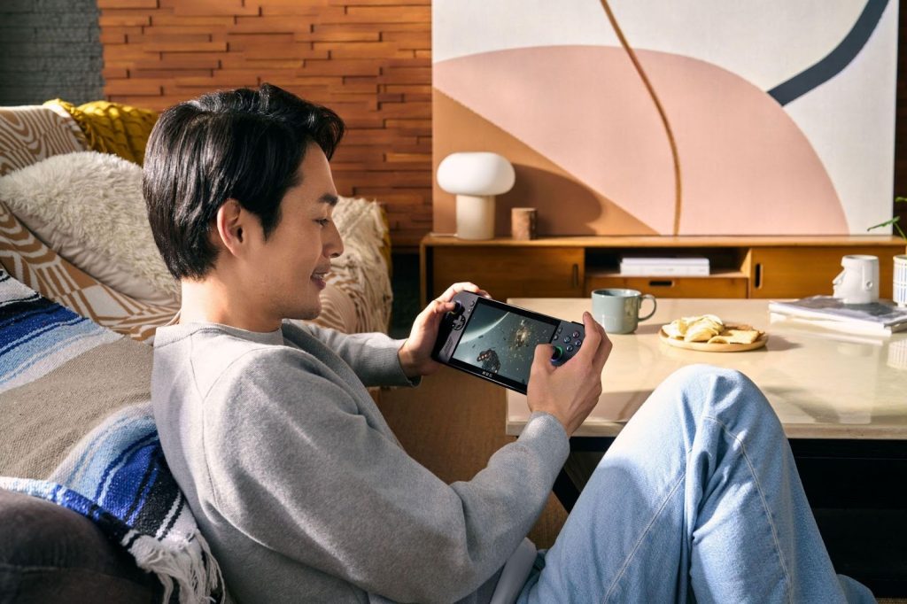 Homem sentado no sofá segurando o console portátil ROG Ally X com um jogo na tela, relaxando na sala.