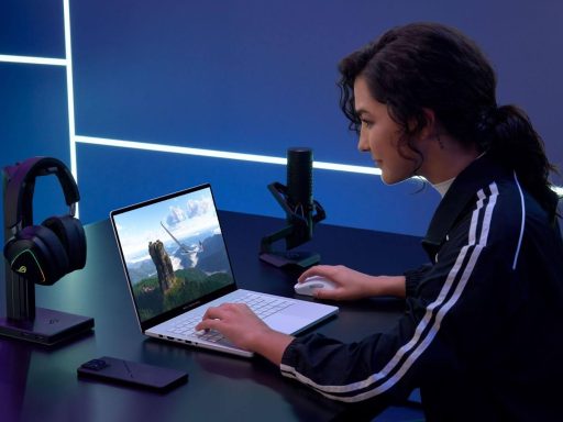 Uma jovem de cabelos escuros e jaqueta esportiva utiliza um notebook ASUS ROG Zephyrus branco em uma mesa de setup gamer.