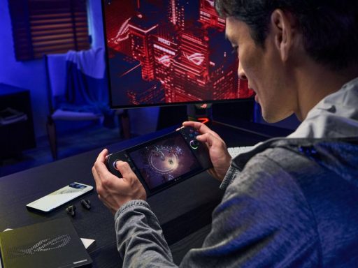 Pessoa jogando em um console portátil ROG Ally X em uma mesa gamer, com monitor e smartphone ASUS ROG ao fundo.