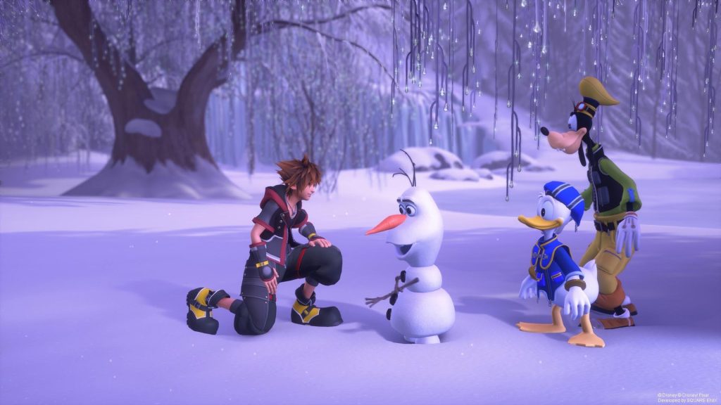 Sora ajoelhado na neve conversando com o boneco de neve Olaf, de Frozen, enquanto Pato Donald e Pateta observam em cenário de inverno arborizado.